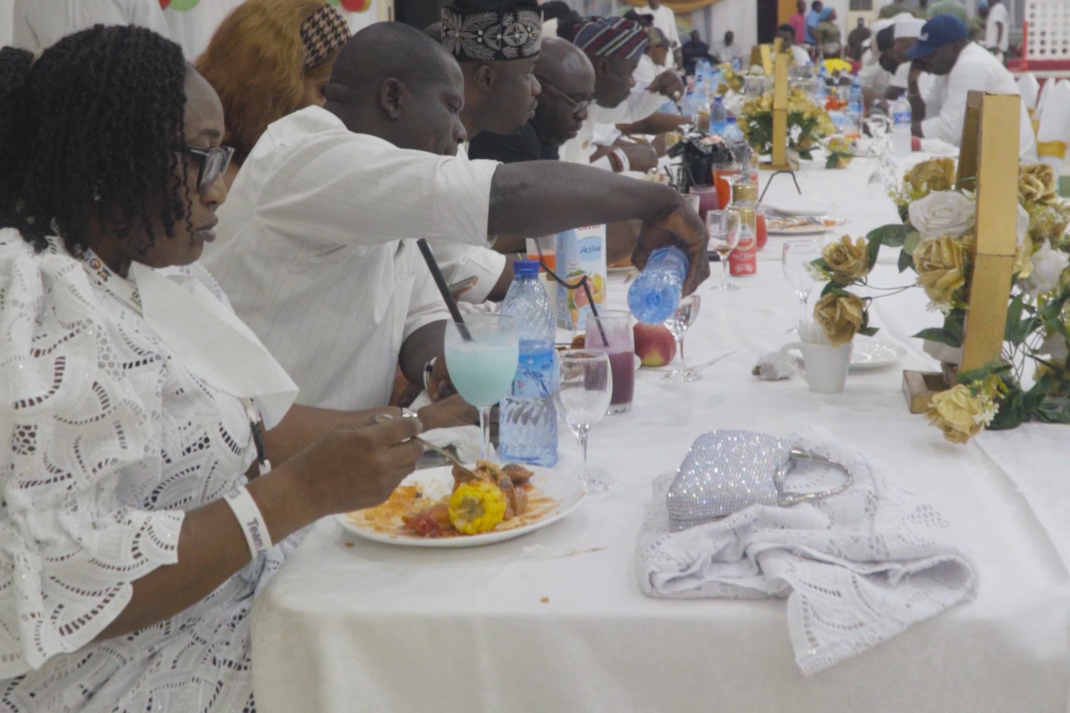 Guests dressed in white seated at a long dinner table in a decorated hall